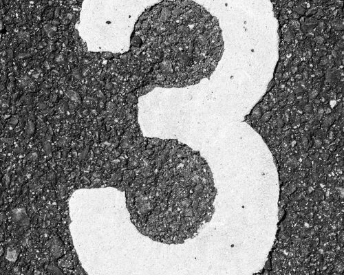Vertical shot of a white number three on asphalt ground